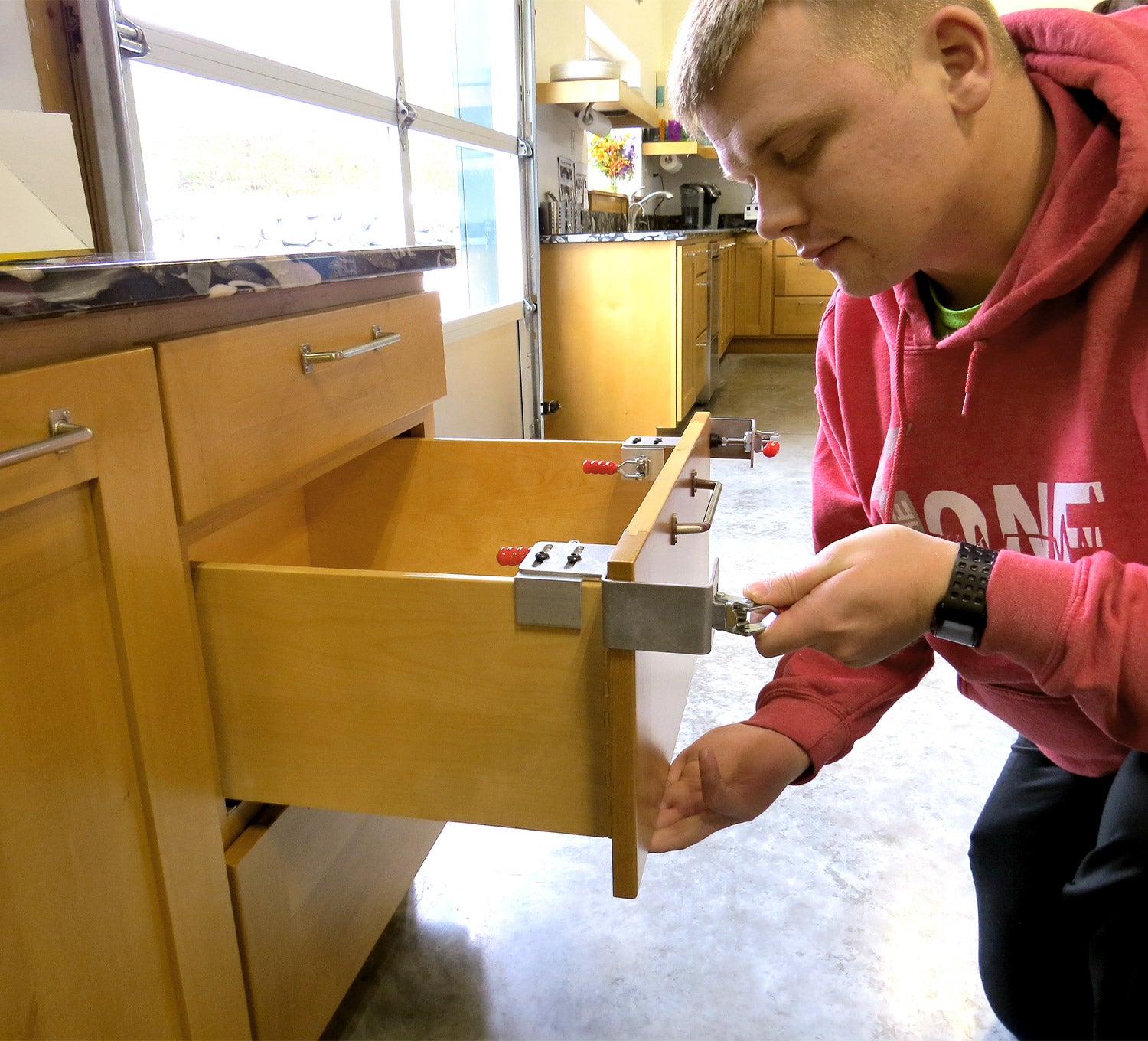 Man using drawer front clamps to secure a drawer front in a kitchen setting, showcasing the clamps in action.
