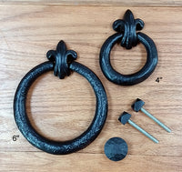 Fleur de Lis door knockers in two sizes, 6-inch and 4-inch, with mounting hardware included on a wooden surface.
