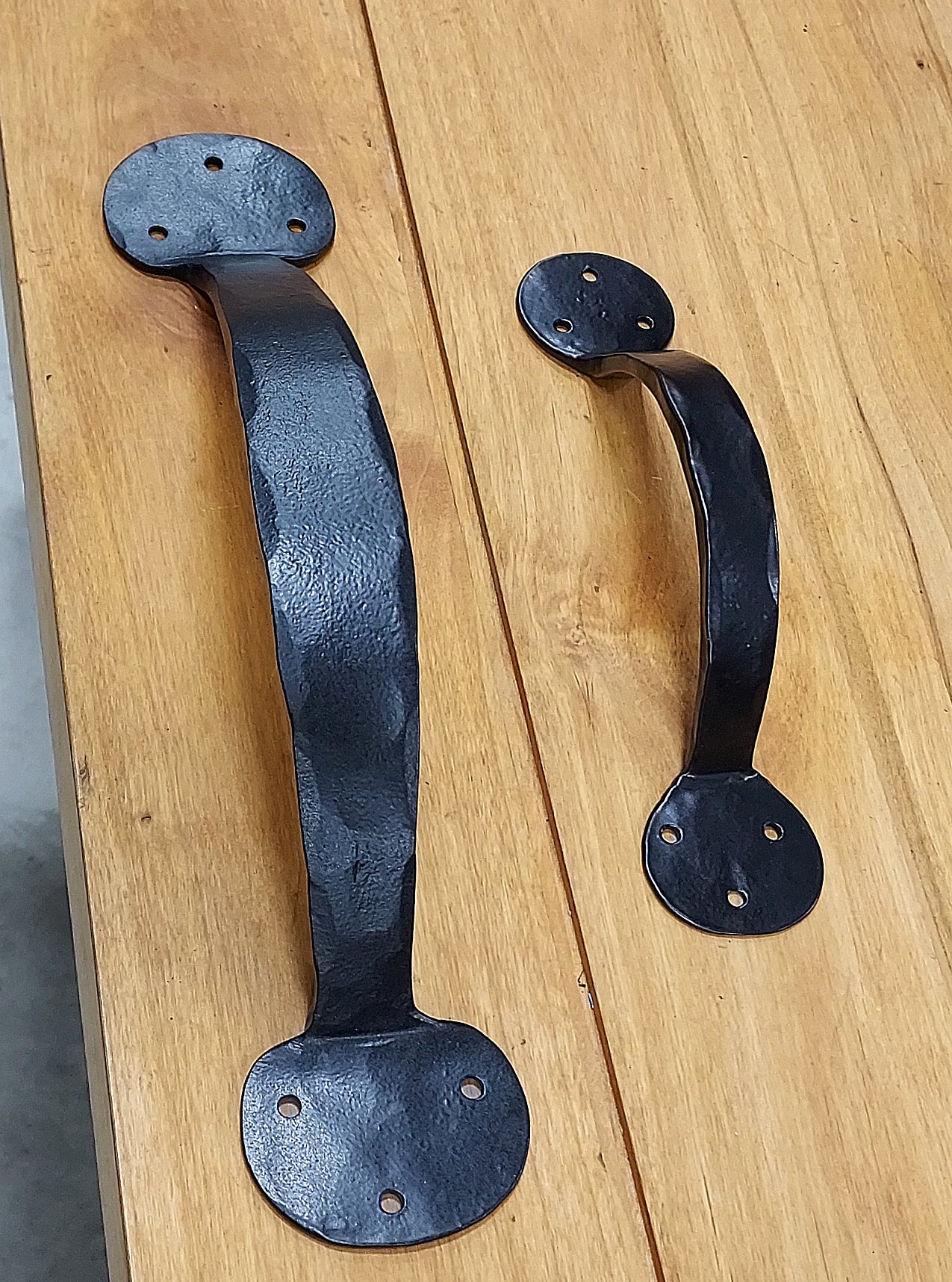 Bean style door handles in two sizes, featuring a rustic finish and exclusive head screws, displayed on a wooden surface.
