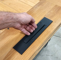 Plain rectangular barn door handle and matching finger pull set displayed on a wooden surface with a hand reaching towards it.