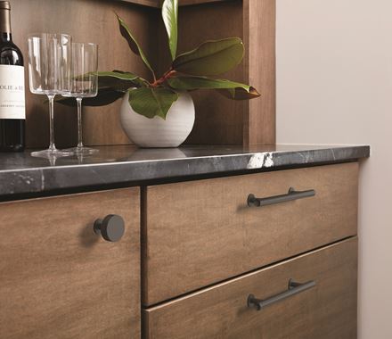 Matte black stainless steel cabinet knob from the Radius Series, 1-1/4 inch, displayed on a wooden drawer.
