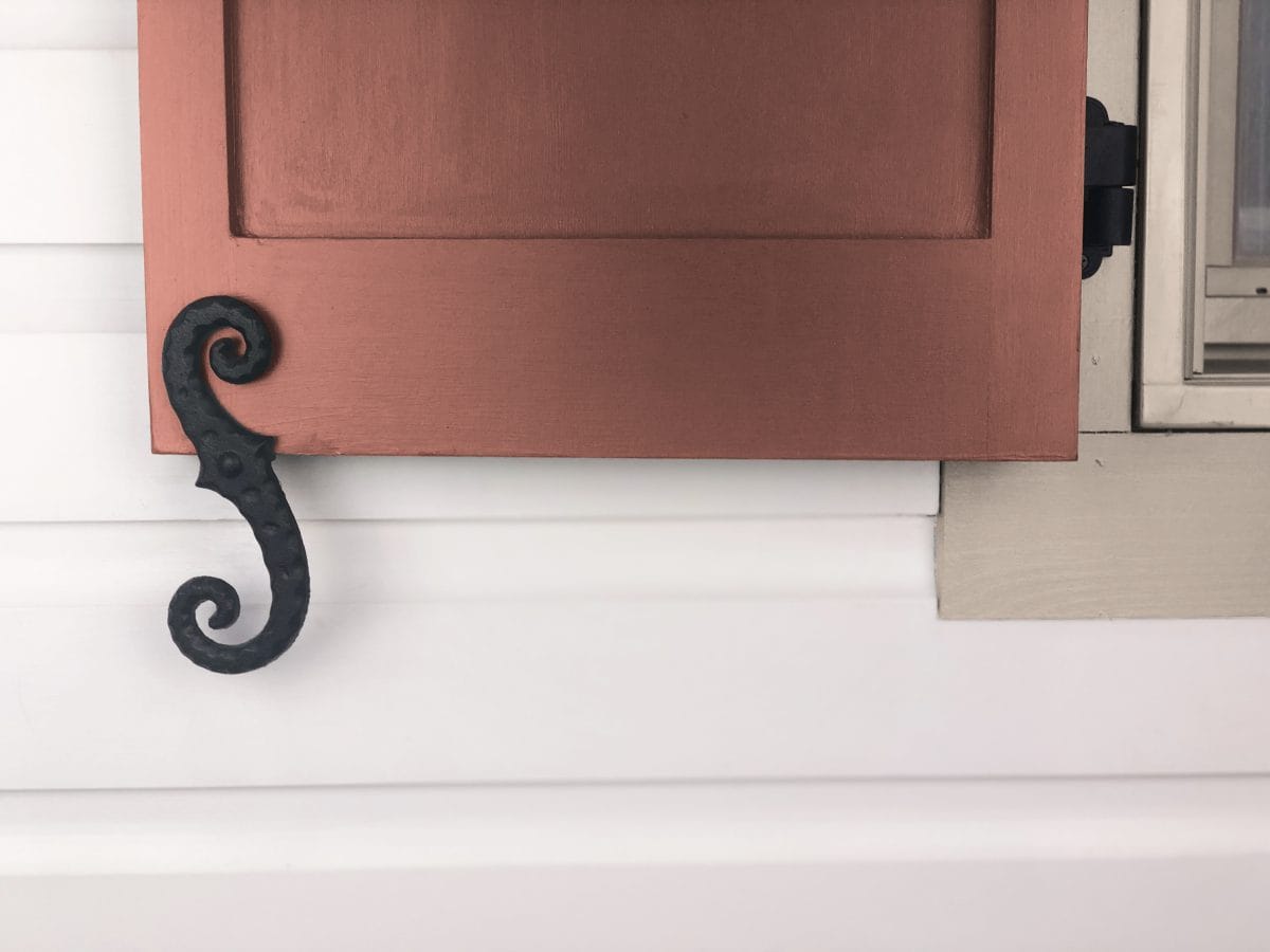 Black powder-coated cast iron faux shutter dogs with stippled scroll design, measuring 6-3/4 inches, sold in pairs.