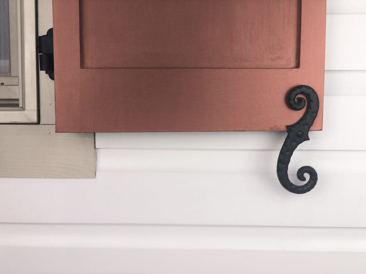 Black powder-coated cast iron faux shutter dog tieback in stippled scroll design, measuring 6-3/4 inches, sold in pairs.