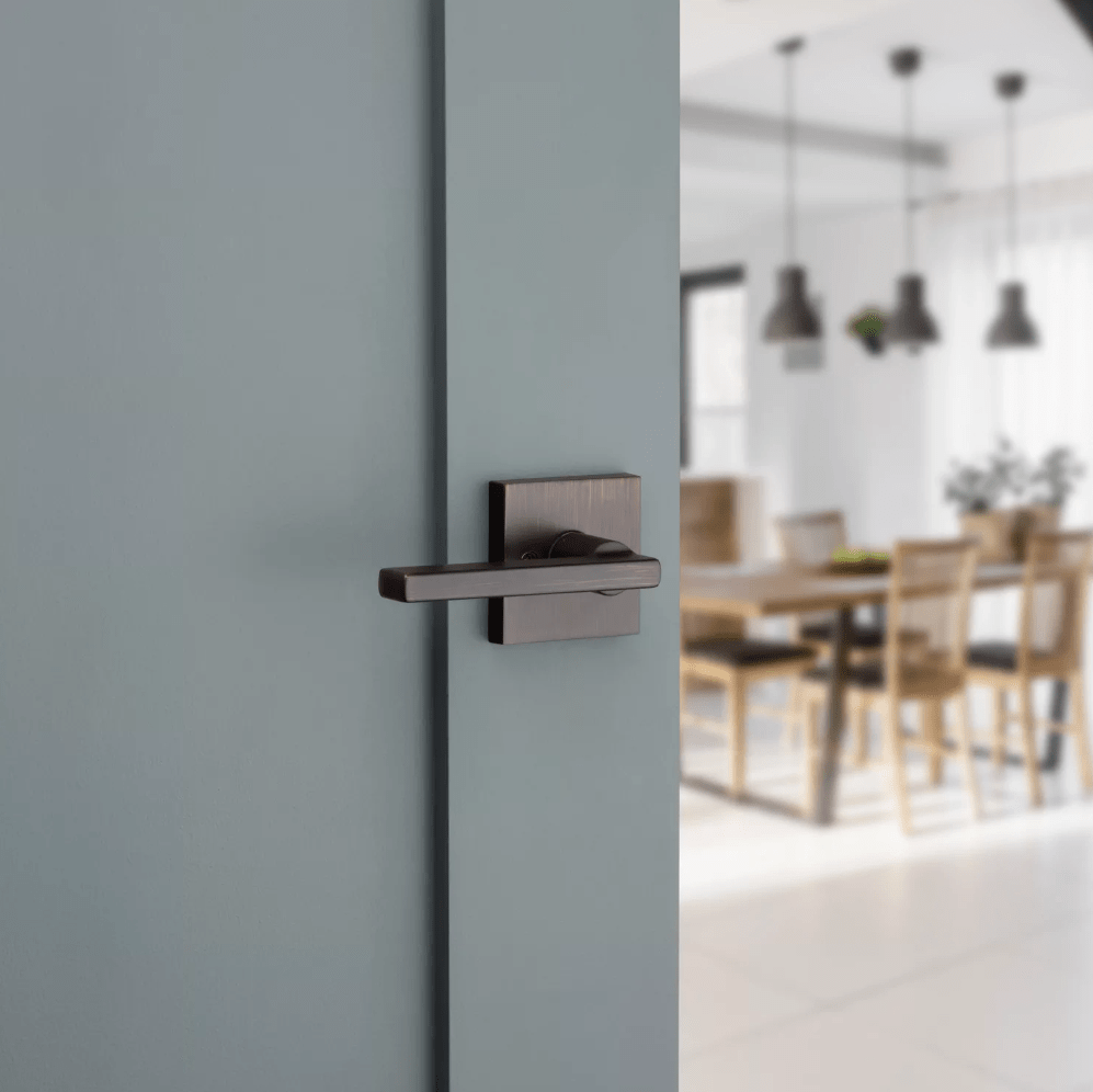 Kwikset Halifax square non-locking passage door lever in venetian bronze finish mounted on a light blue door.