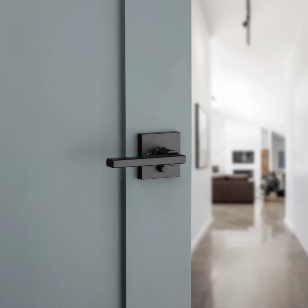 Kwikset Halifax square privacy door lever in iron black finish, designed for residential use, shown on a light blue door.