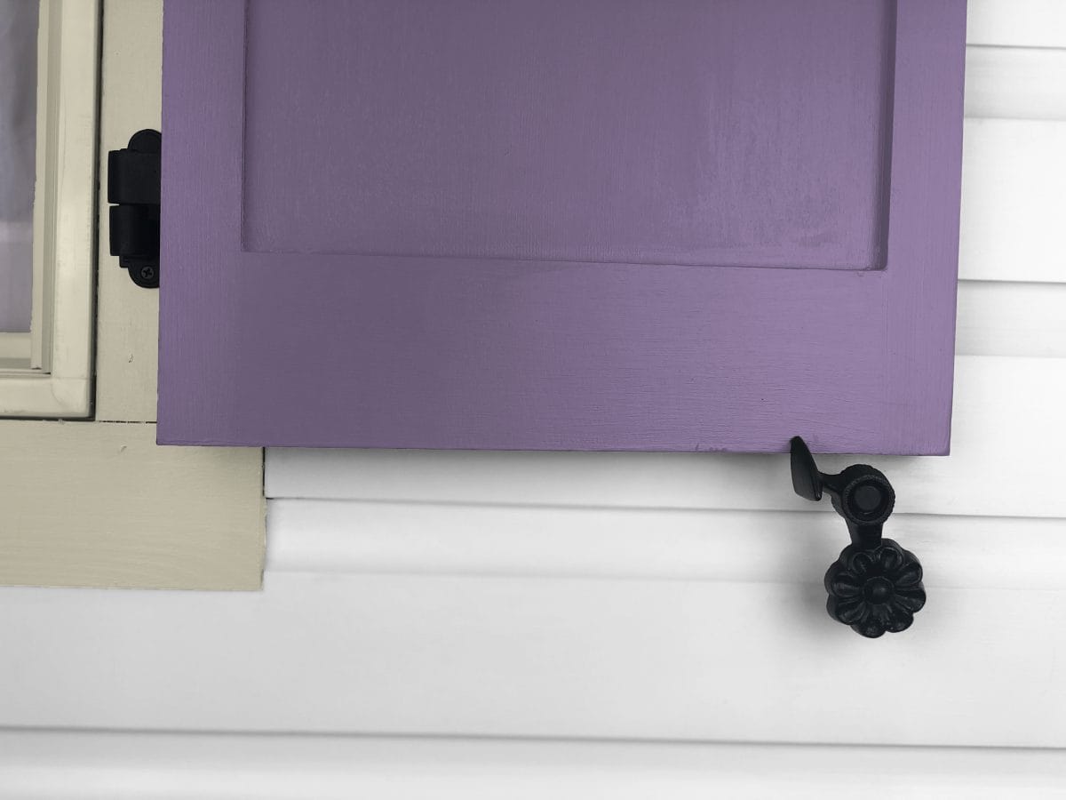 Black cast iron shutter dogs with flower design, 4-1/2 inches, securing a purple shutter, sold in pairs.