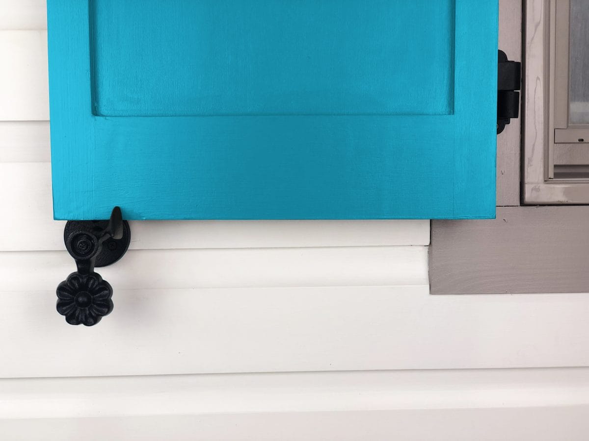 Black powder-coated cast iron shutter dogs with flower design, 4-1/2 inches, mounted on a blue shutter. Sold in pairs.
