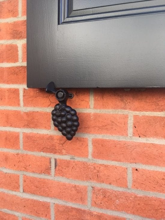 Black powder-coated cast iron shutter dogs in a grape design, measuring 6-1/4 inches, sold in pairs.