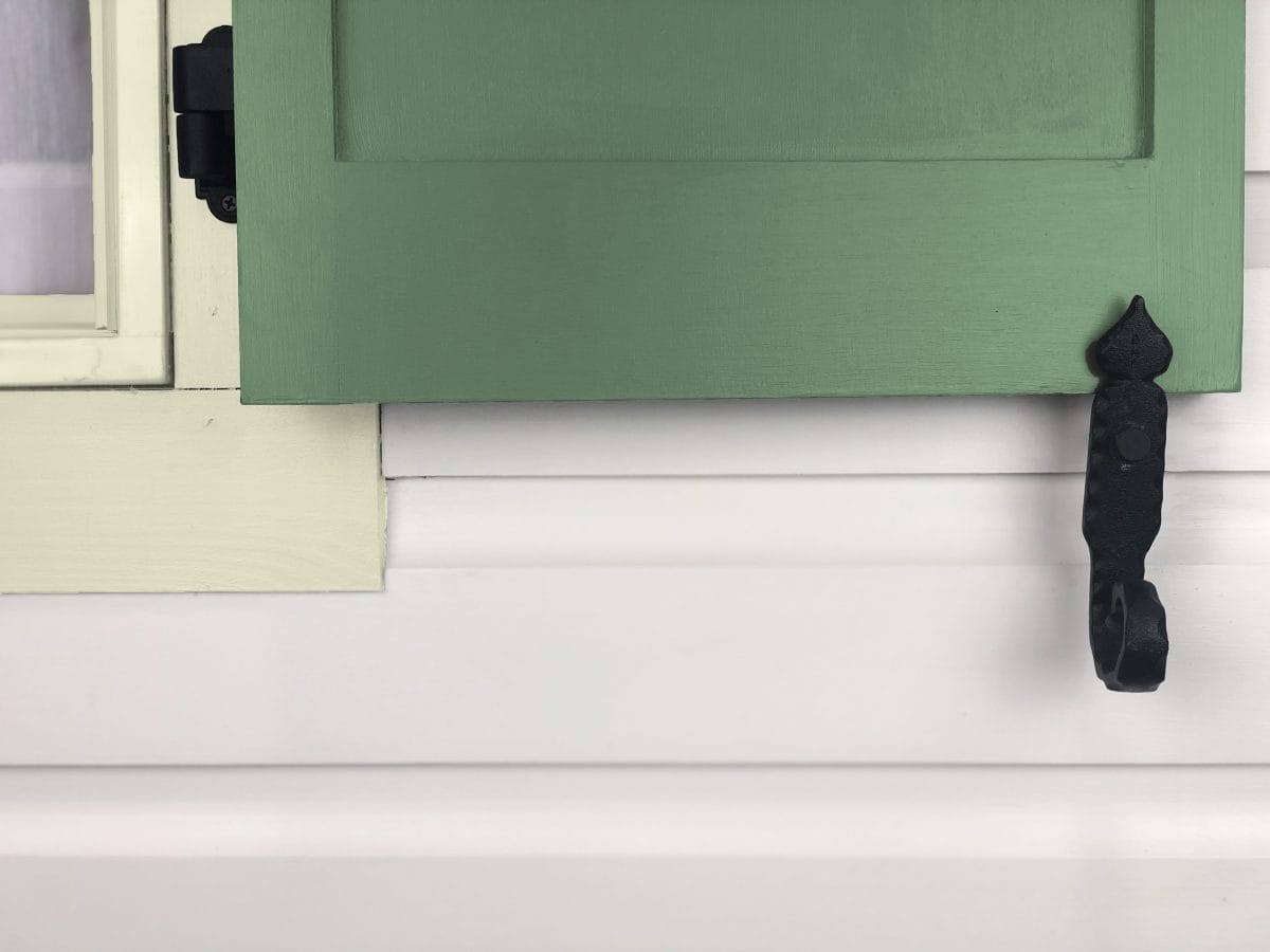Black powder-coated cast iron rat tail shutter dogs, 6-1/4 inches, securely holding a green shutter, sold in pairs.
