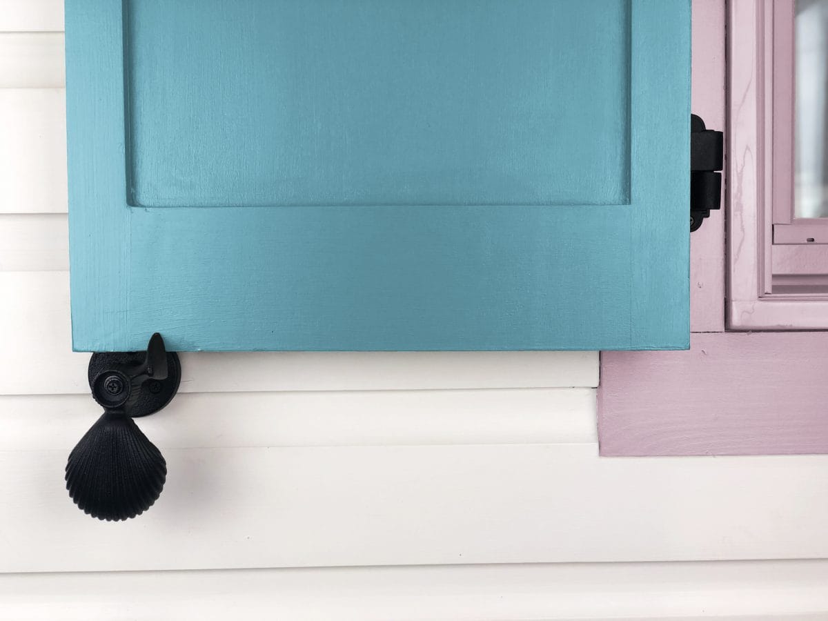 Black cast iron shutter dogs with shell design, 5-1/4 inches, securing a blue window shutter, sold in pairs.