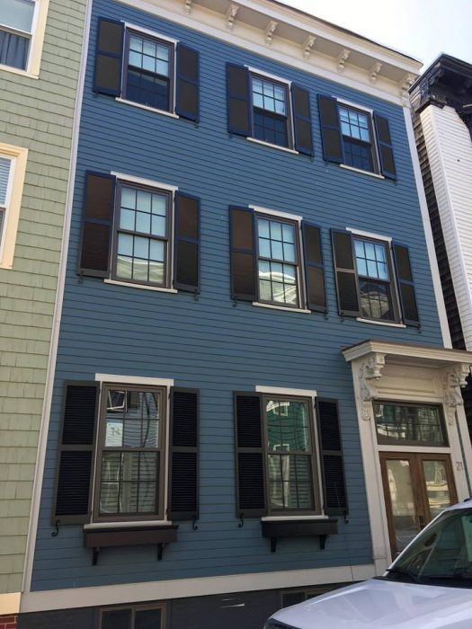 Black cast iron shutter dogs and tiebacks in a value pack, enhancing the charm of a blue house with shutters.