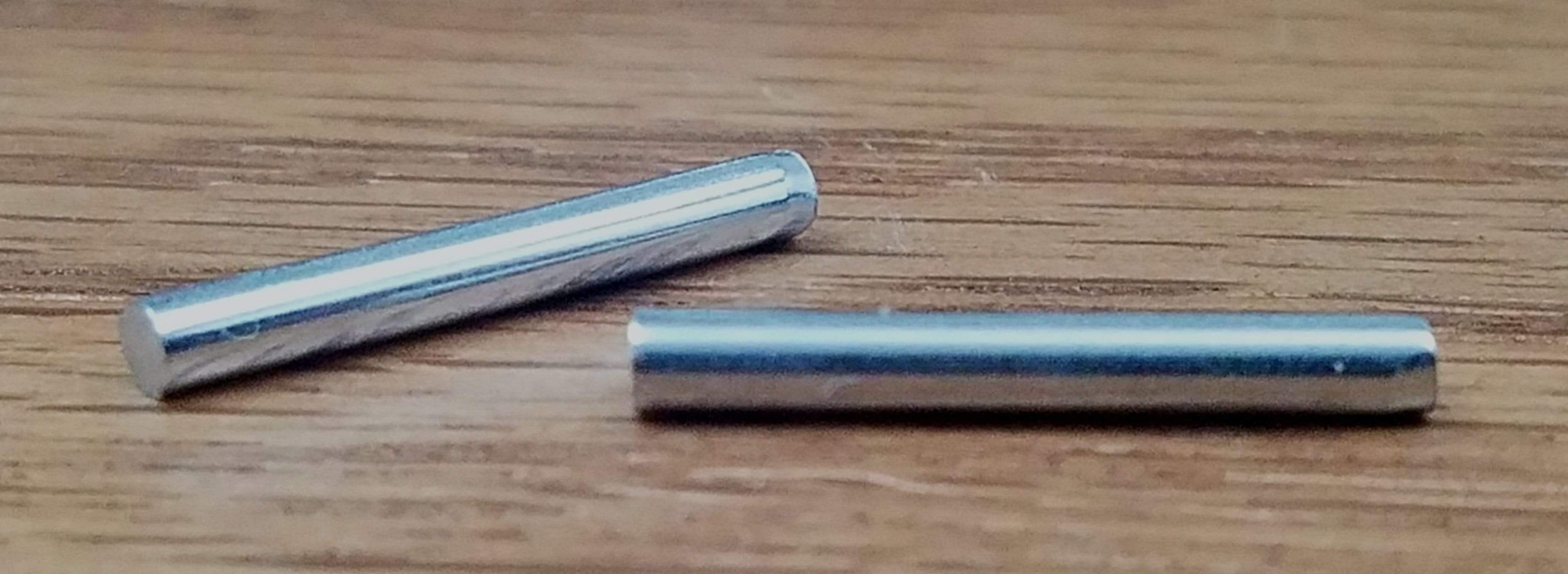 Two silver spring hinge tension pins on a wooden surface, designed for hinge replacement and repair.