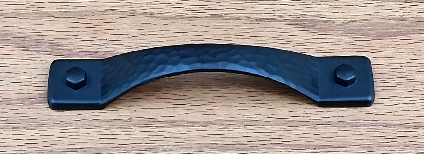 Rustic hammered drawer pull in matte black finish, featuring a curved design with two hexagonal bolts.