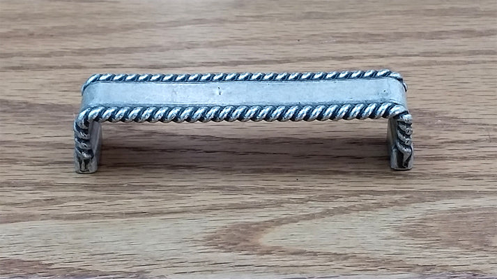 Old silver drawer pull with a decorative rope edge design, sold individually for cabinets and furniture.