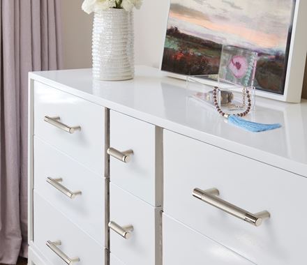 Polished nickel cabinet knobs from the Esquire Series, 2-5/8 inches, displayed on a white dresser with decor.