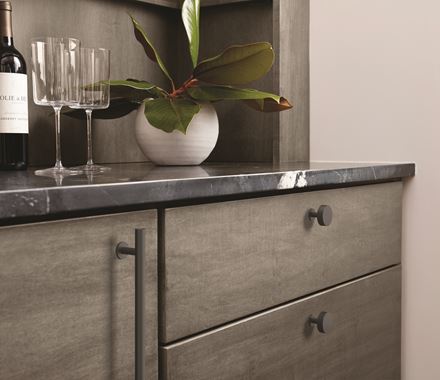 Matte black stainless steel cabinet knob from the Radius Series on a modern gray cabinet with a marble countertop.