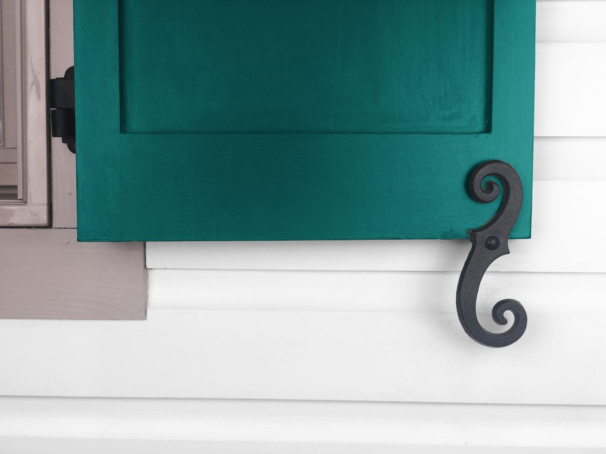 Black powder-coated cast iron faux shutter dogs with a beveled smooth scroll design, measuring 6-3/4 inches, displayed on a teal shutter.