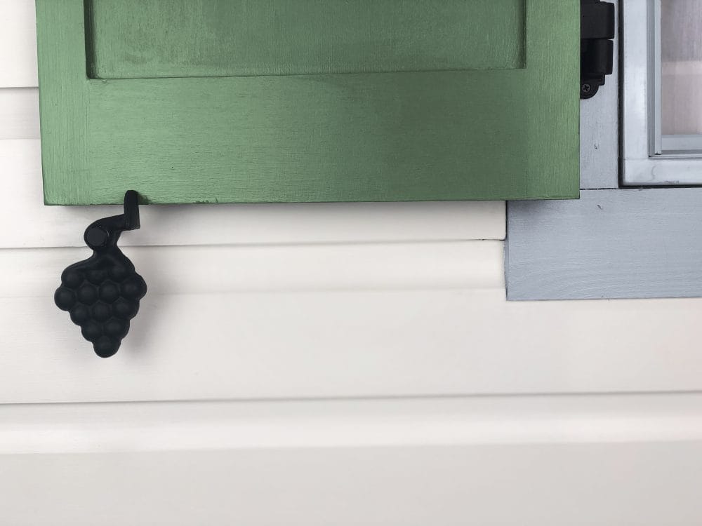 Black powder-coated cast iron shutter dog tieback in JP Style #30-L Grape design, measuring 5-1/2 inches, sold in pairs.
