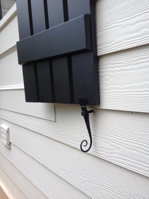 Black powder-coated forged steel shutter dogs, 6-inch English rat tail design, securely holding a shutter in place.