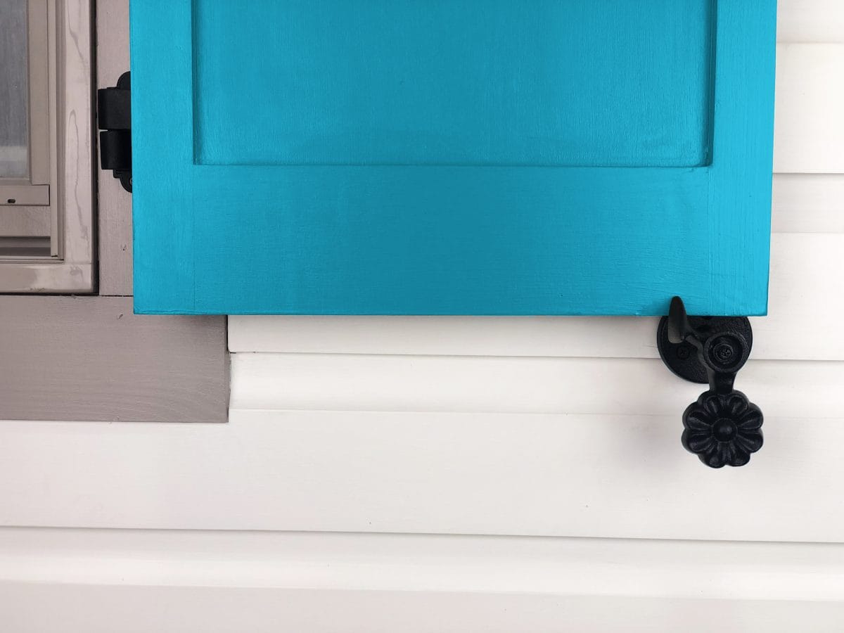 Black powder-coated cast iron shutter dogs in flower design, 4-1/2 inches, securing a blue shutter. Sold in pairs.