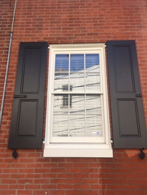Black powder-coated cast iron shutter dogs in grape design, 6-1/4 inches, displayed on a window with shutters.