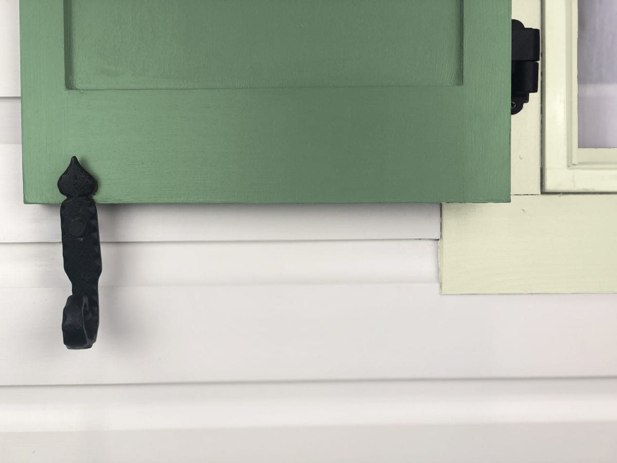 Black powder-coated cast iron shutter dogs in rat tail design, 6-1/4 inches, securing a green shutter. Sold in pairs.