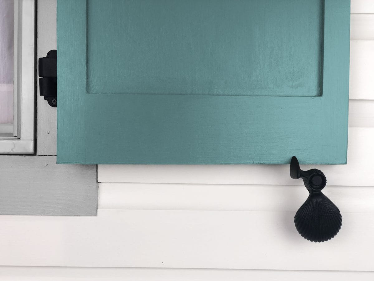 Black cast iron shutter dogs with shell design, 5-1/4 inches, used to secure open shutters, sold in pairs.