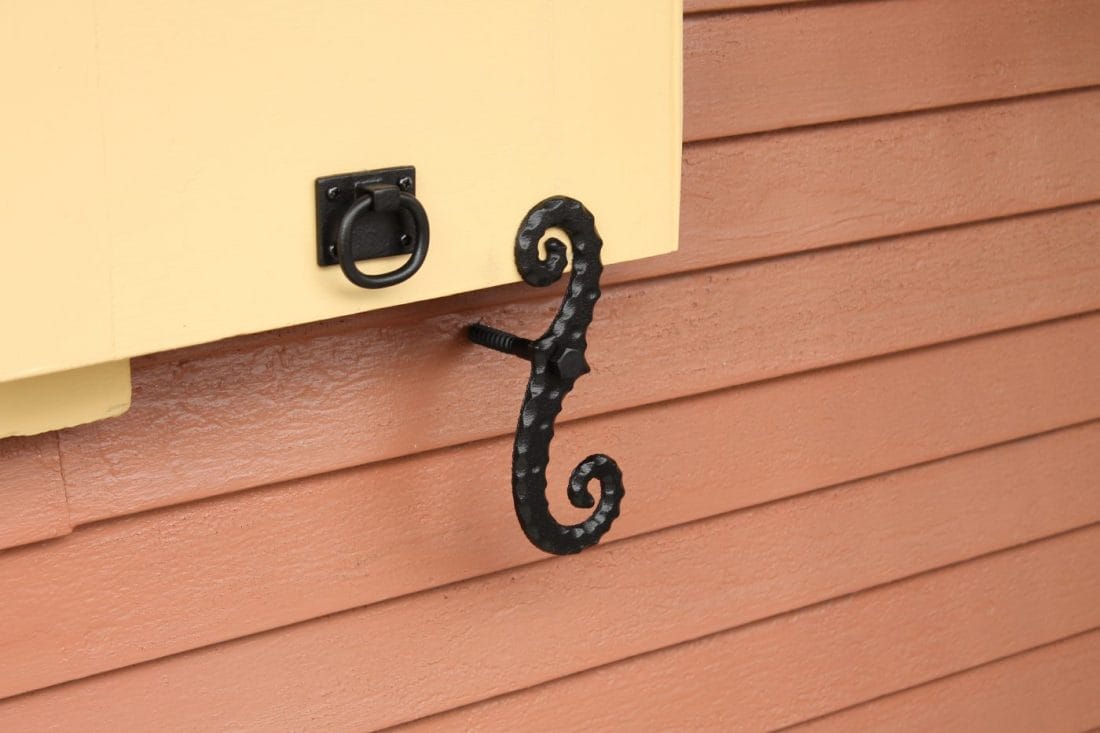 Black cast iron shutter dogs tiebacks in a scroll design, 6-3/4 inches, securely holding a shutter open.