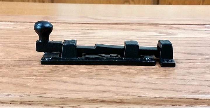 Small surface slide bolt for gates with a round ball handle, featuring a black powder coat finish. Sold individually.