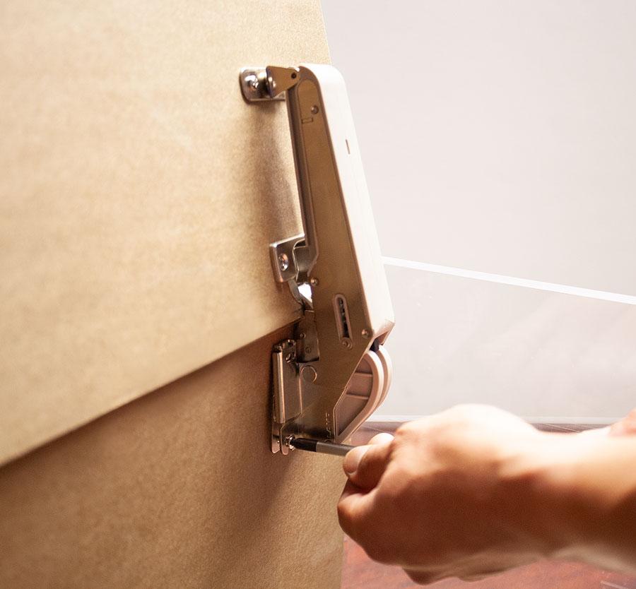 Soft close lid stay with lift assist mechanism, shown being installed on a cabinet for smooth operation.